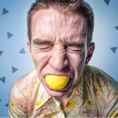 man with lemon in mouth making a bad face